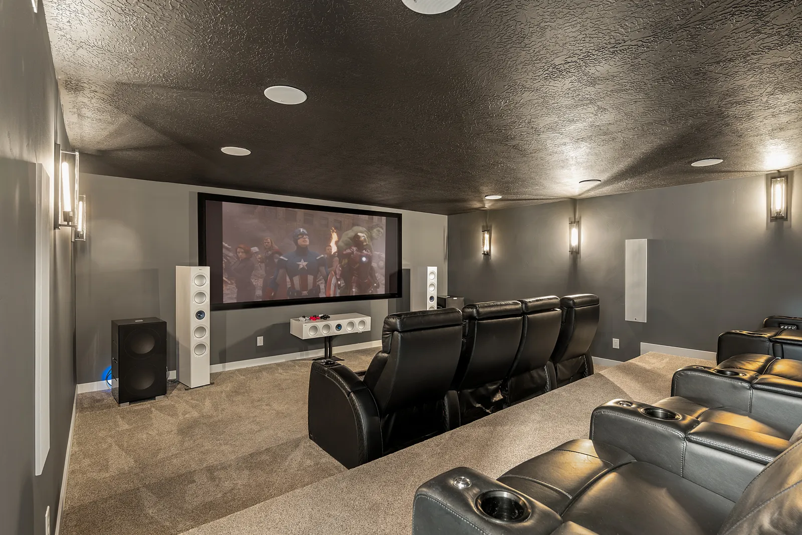 Finished dedicated home theater built by our team — screen lit, reference tower speakers, tiered leather seating