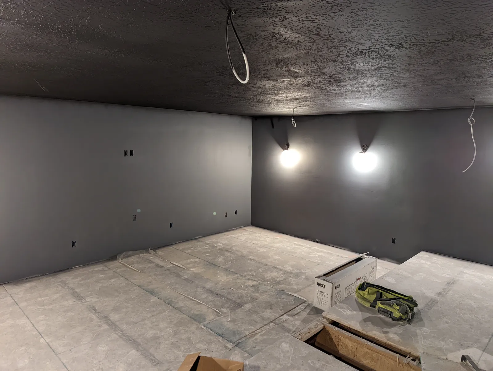 Drywalled theater room painted dark with sconces mounted and speaker wiring staged from the ceiling